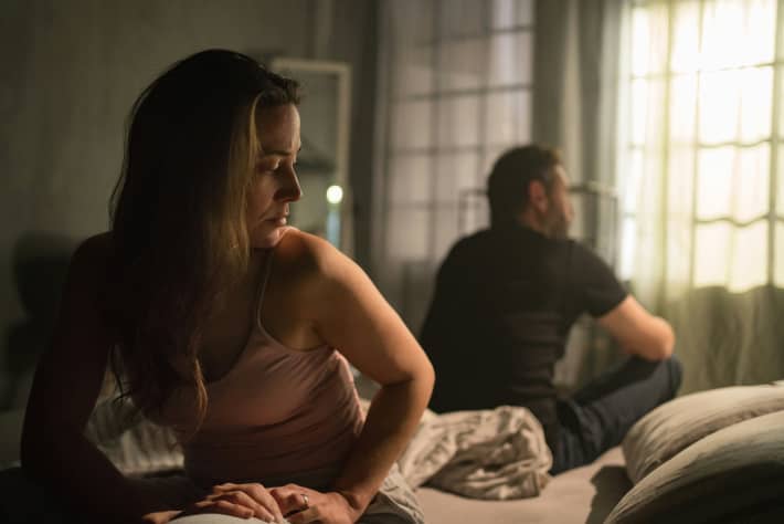 Couple in disagreement sit back to back on a bed.
