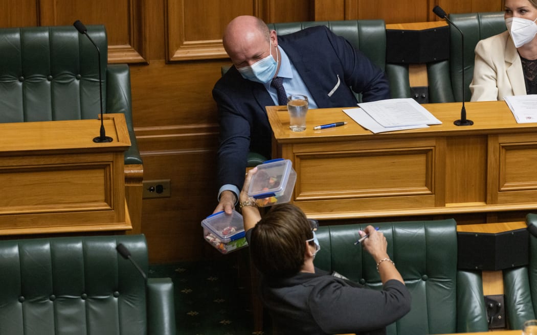 National Party junior whip Maureen Pugh undertaking a traditional whip duty, keeping her party's MPs in the debating chamber well supplied with snacks. Here she swaps lolly boxes with National MP David Bennett.s.