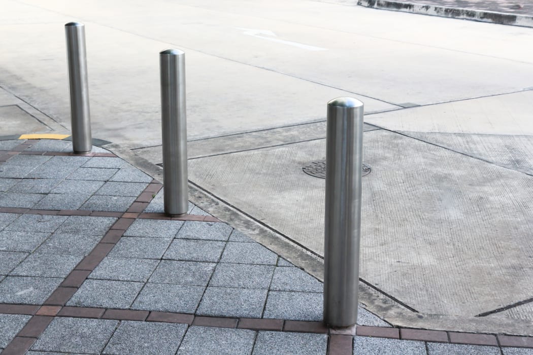 Stainless Steel bollards on grey stone pavement of car park.