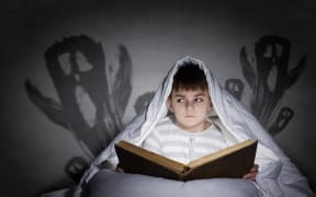 A photo of a boy reading in bed with images of ghosts behind him