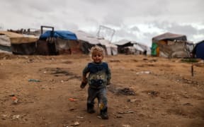 Displaced Palestinian children are seen outside a tent along the seafront in Gaza City, on January 9, 2026.