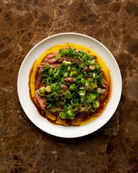 A plate of charcoal steak topped with green onions by Newton-based Bar Magda.