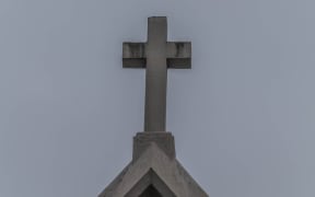 Catholic church steeple with cross on top, sky as background.