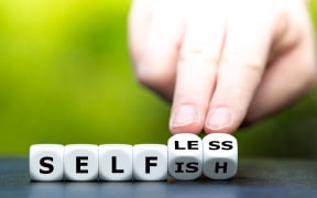Hand turns dice and changes the word "selfish" to "selfless"No caption.