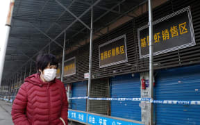 A woman walks in front of the closed Huanan wholesale seafood market, where health authorities say a man who died from a respiratory illness had purchased goods from, in the city of Wuhan.
