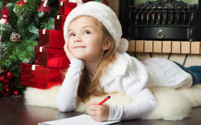 Girl in Santa hat writing letter for Christmas.