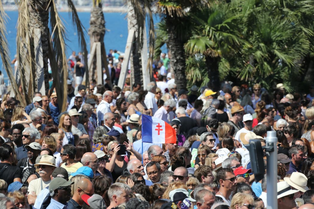 A man holds a French flag showing the Cross of Lorraine as people gather to observe a minute silence on the Promenade des Anglais in Nice on July 18, 2016, in tribute to victims of the deadly Nice attack on Bastille day.