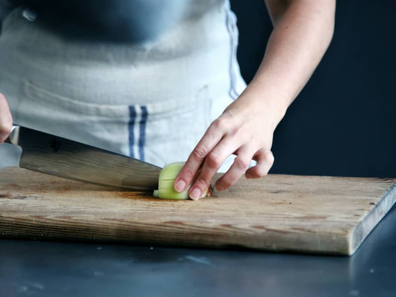 A person chops a cucumber on a wooden chopping board.