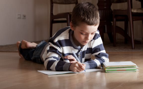 A primary school student does his homework on the floor at home.