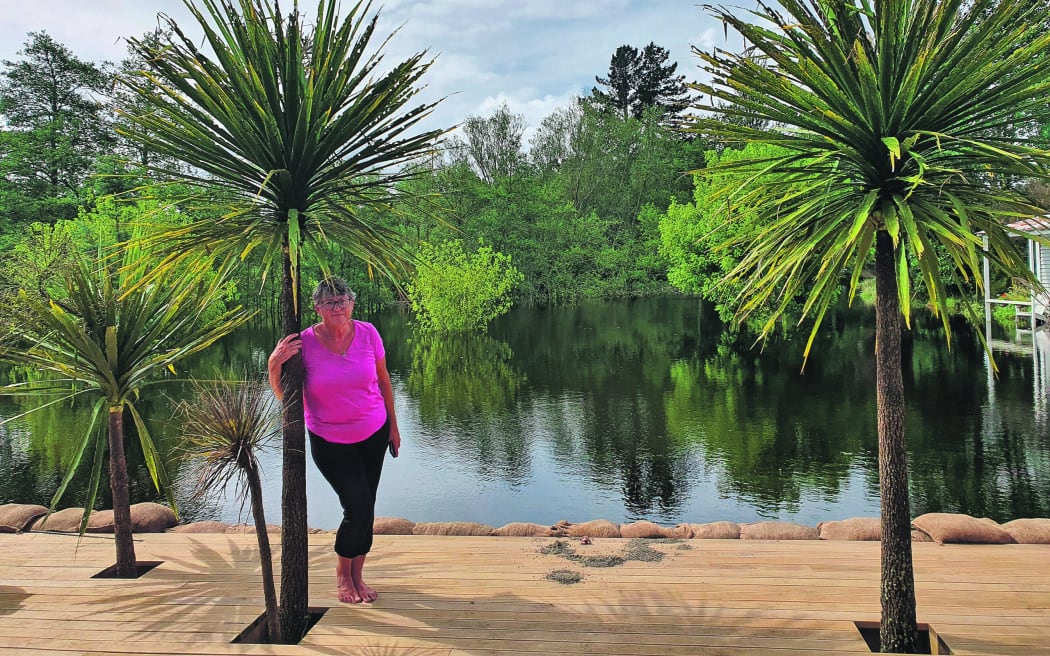 Christine McDonald stands on the deck of her villa home on Manawahe Road overlooking what used to be her lawn and some half-drowned trees.