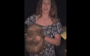 This screenshot of a video posted by Sam Jones shows the US influencer picking up a wild baby wombat and holding it for the camera.