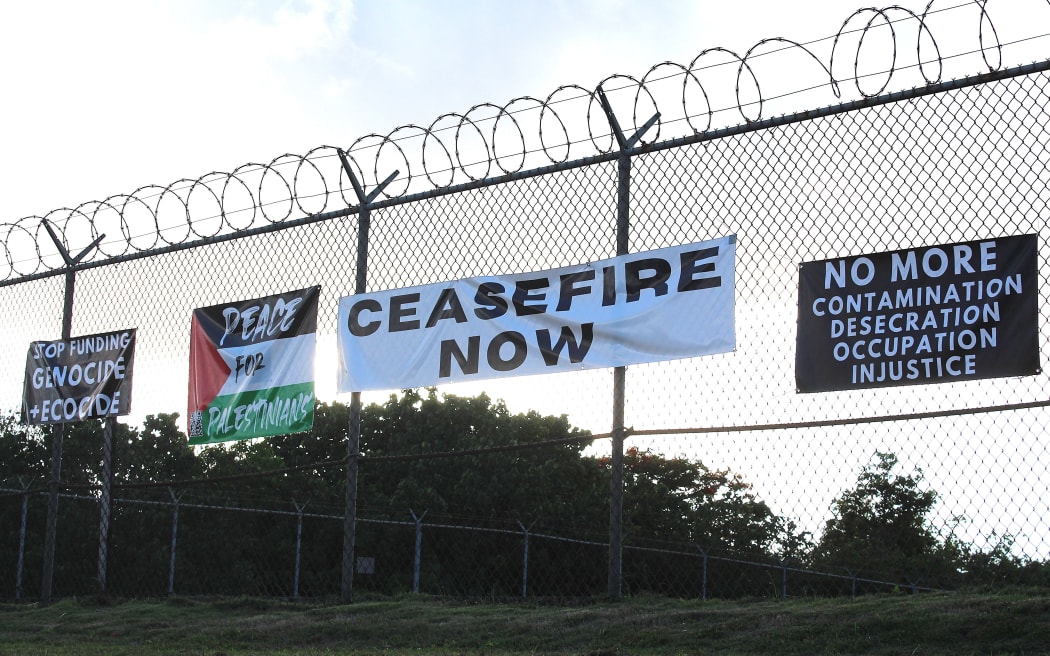 Signs calling peace for Palestine and an end to violence are displayed along a chain-link fence in Guam for the 2025 No King's rally.