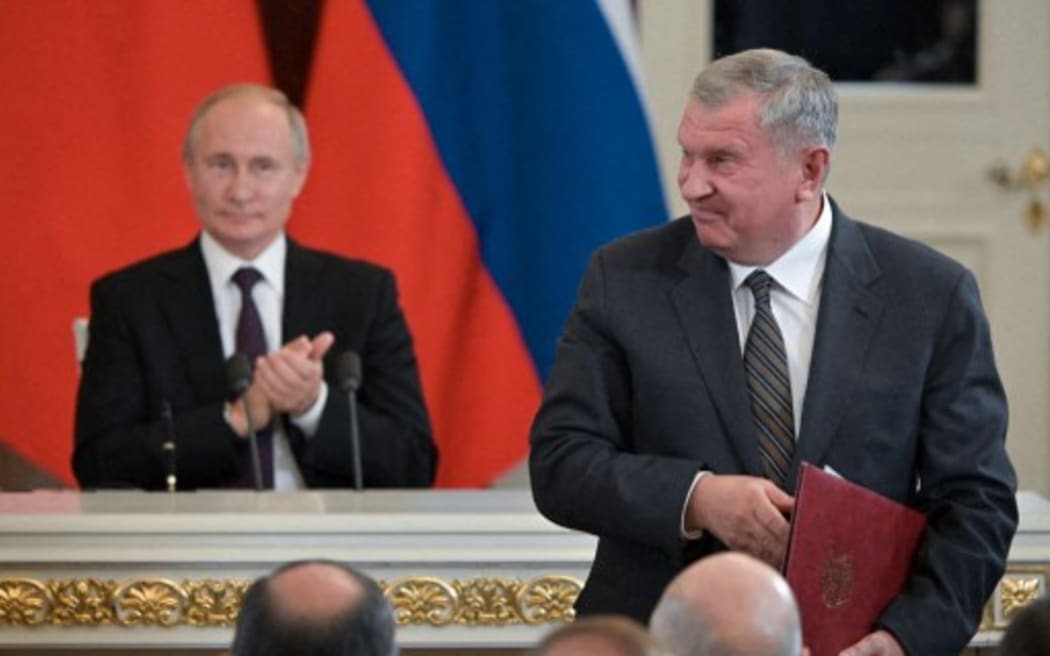 Rosneft chief executive Igor Sechin smiles during a signing ceremony, with Russian President Vladimir Putin seen in the background.