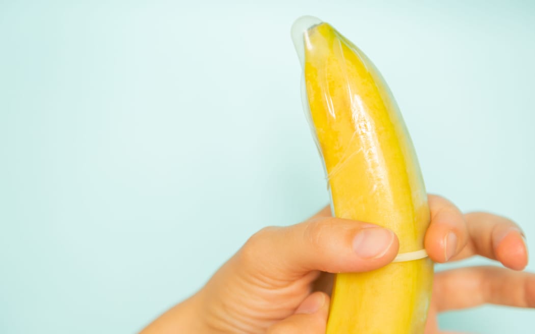 Sex education concept - hands putting condom on banana pastel background, copy space