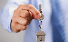 A man in a business shirt holds out a set of house keys.