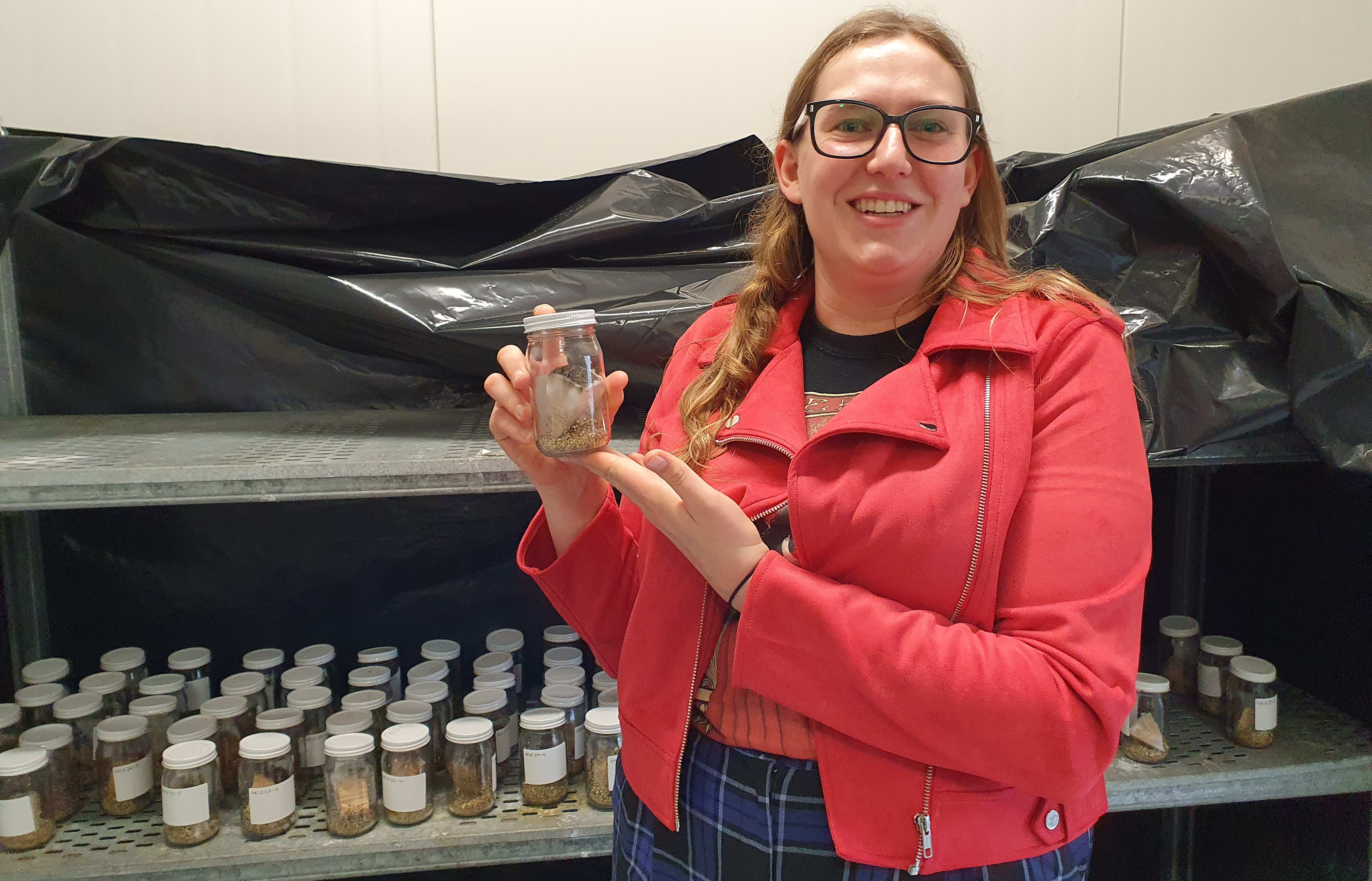 A photo of Genevieve Early in the University of Canterbury Mushrrom house with the Armillaria fungus samples grown for her research.