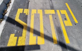 The bright yellow letters painted on Te Atatū Road spell "bus sotp.".