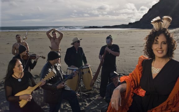 Moana and The Tribe with instruments, on a beach.