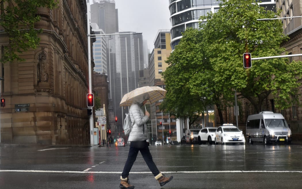 A woman shelters from the rain under an umbrella while crossing a street in Sydney on October 6, 2022. (Photo by Muhammad FAROOQ / AFP)