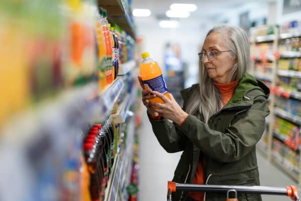 Person reads the label on an orange juice bottle at a supermarket.