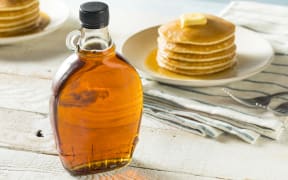 Maple syrup with some pancakes in the background.