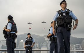 Police officers standing guard in front of Helicopters operated by the Hong Kong Government Flying Service with the National Flag of China and the HKSAR Flag hanging below it flying pass Victoria Harbour on October 1, 2023 in Hong Kong, China. Today marks China's National Day (Photo by Vernon Yuen/NurPhoto) (Photo by Vernon Yuen / NurPhoto / NurPhoto via AFP)