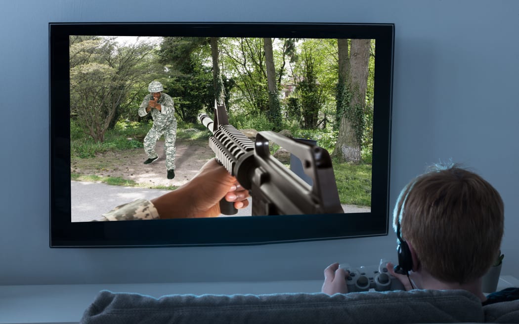 A photo of a Boy Sitting On the Sofa Playing an Action Game involving guns On Television