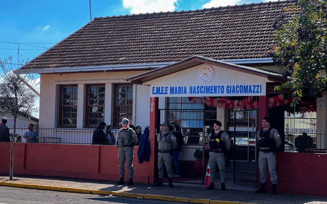 Police officers stand guard at the entrance of the Municipal School Maria Nascimento Giacomazzi after a 16-year-old teenager entered the school, killed a child, and wounded two people in Estacao, Rio Grande do Sul State, Brazil, on July 8, 2025. (Photo by Andrei NARDI / Grupo Sideral de Radios / AFP)