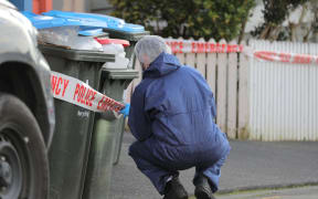 A police investigator looks closely at a set of rubbish bins on Renall St