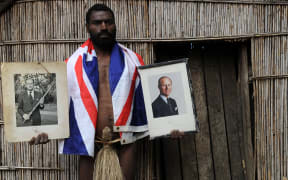Sikor Natuan, the son of the local chief, holds two official portraits (one holding a pig-killing club) of Britain's Prince Philip in front of the chief's hut in the remote village of Yaohnanen on Tanna.