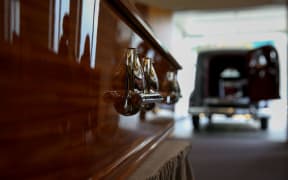 Close up of side of shiny wood coffin with hearse in the background