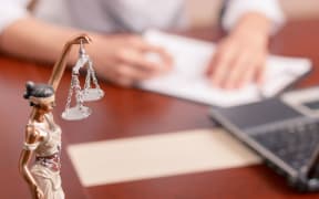 Follow the law. Professional lawyer sitting at the table and signing papers with justice statue standing on surface in forefront.