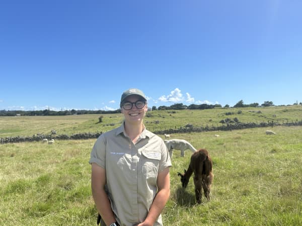 Picture of a woman smiling at the camera, with two llamas in the background.