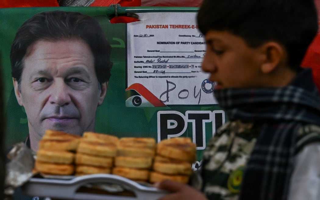 A child walks past a poster showing Pakistan’s jailed former prime minister Imran Khan at a market a day after Pakistan's general election in Lahore on February 9, 2024.  (Photo by Aamir QURESHI / AFP)