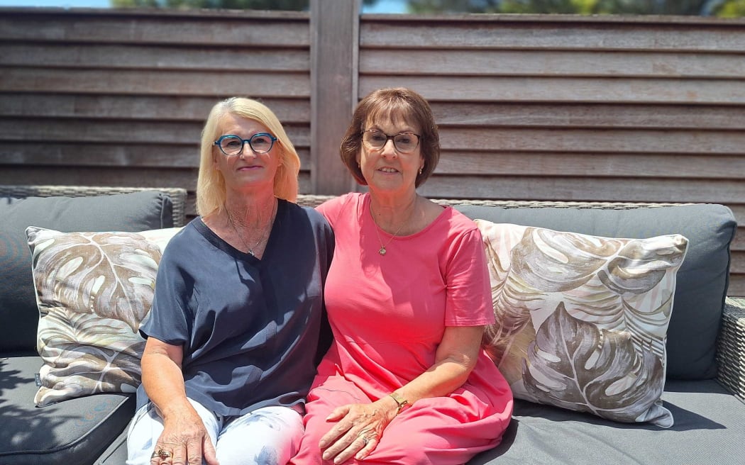 Two women sit side by side on outside couch in sunshine