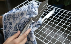 A person uses a tea towel to wipe a stainless steel knife.