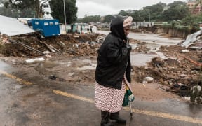 A woman in a drenched raincoat walks pass the Quarry road informal settlement outside Durban on April 18, 2022 as rain begins to fall once again after winds, heavy rainfall and mudslides destroyed many homes and infrastructure last week.