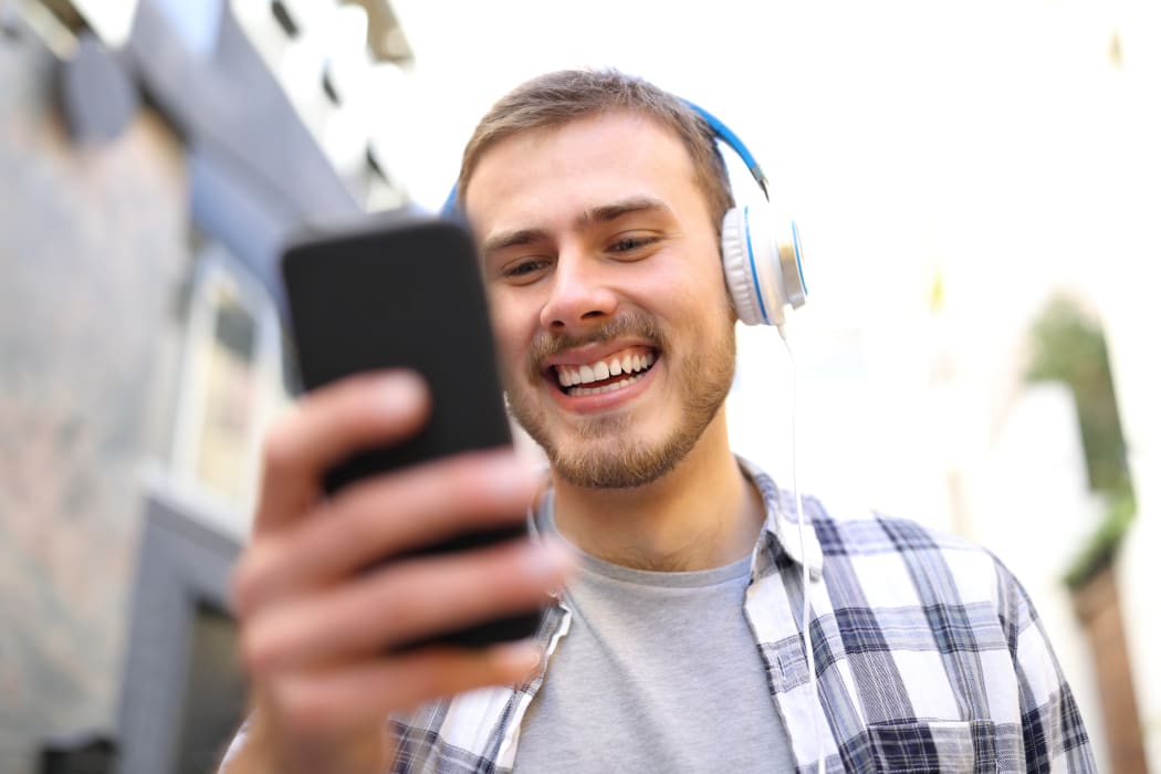 Portrait of a happy man listening to the music with smart phone walking in the street