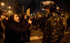 A woman attending a candlelight vigil, in memory of the victims of Ukraine International Airlines Boeing 737, talks to a policeman following the gathering in front of the Amirkabir University in the Iranian capital Tehran on January 11, 2020.