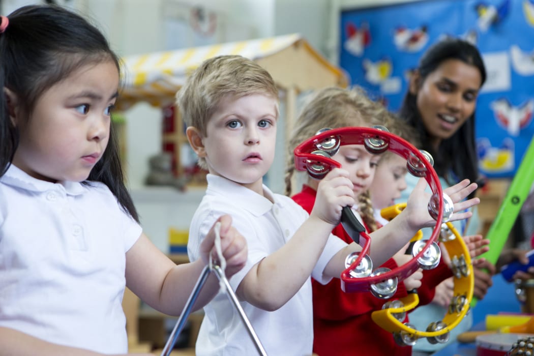 A photo of a young children playing musical instruments. The girl in the foreground looks worried but is joining in.