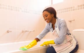 Young woman cleaning bathtub with a cloth