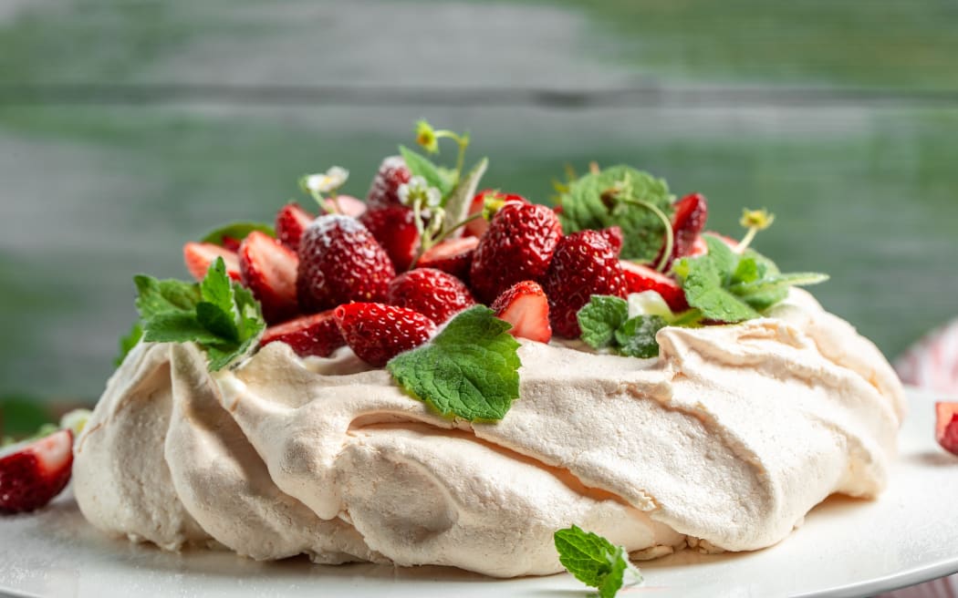 Homemade delicious meringue cake Pavlova with whipped cream, fresh strawberries and mint on wooden background, close up view.