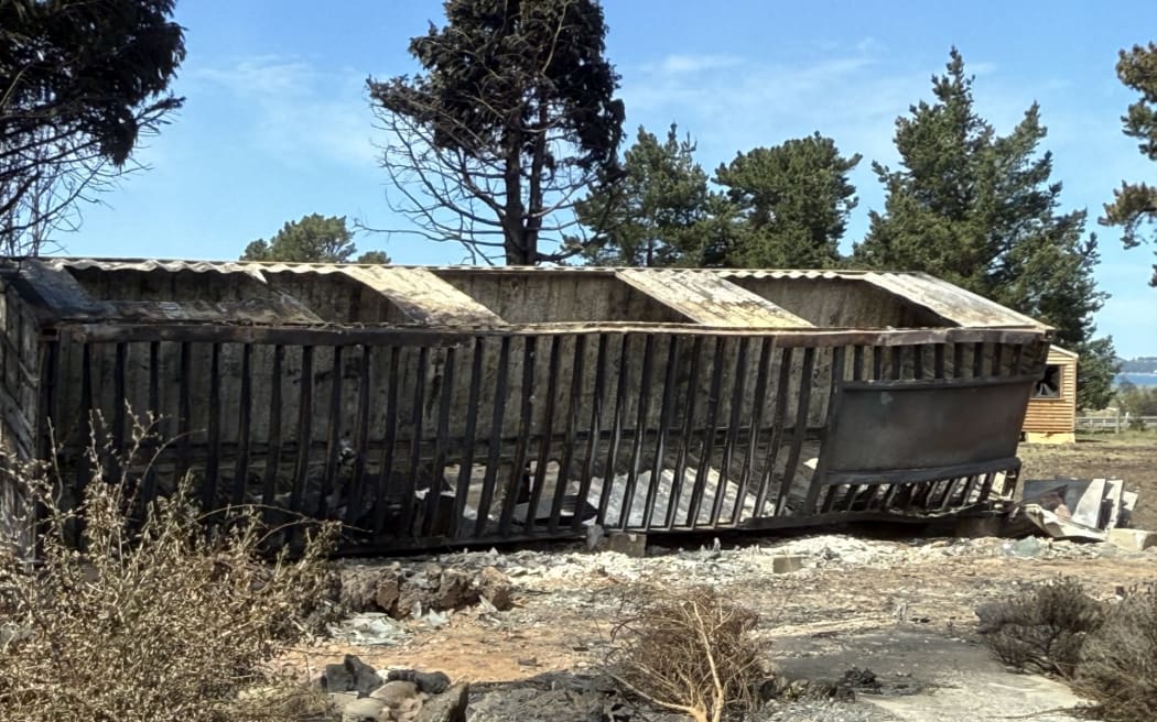 A charred, burnt out shipping container, surrounded by ashes.