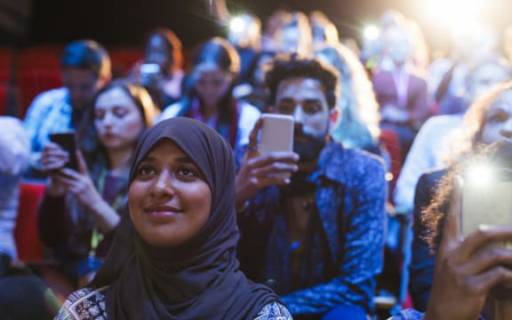 Smiling woman in hijab listening in audience.