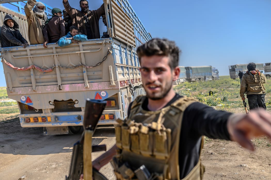 A member of the Kurdish-led Syrian Democratic Forces (SDF) monitors trucks carrying men, identified as Islamic State group fighters who surrendered as they are being transported out of IS's last holdout of Baghuz in Syria's northern Deir Ezzor province.