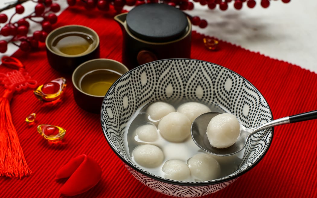 Bowl of tangyuan, tea and Chinese decor on red mat, closeup. Dongzhi Festival