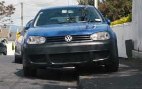 Pedestrians try to use the footpath in Auckland where cars are parking over the kerb.