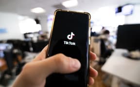 This photograph taken on April 19, 2024 shows a man holding a smartphone displaying the logo of Chinese social media platform Tiktok in an office in Paris (Photo by Antonin UTZ / AFP)
