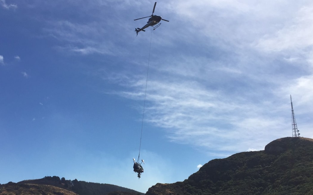 The wreckage of the helicopter that crashed while fighting the Port hills blazes on Tuesday, killing pilot Steve Askin, is airlifted off the hills.