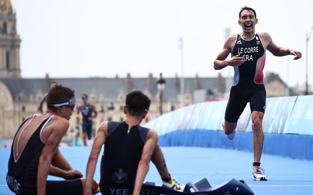 New Zealand's Hayden Wilde (L) sits next to Britain's Alex Yee as France's Pierre Le Corre crosses the finish line in the men's individual triathlon race at the Paris 2024 Olympic Games in central Paris on July 31, 2024. (Photo by Anne-Christine POUJOULAT / AFP)
